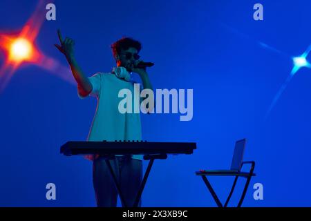 Talented young man, musician captivating the audience in night club, singing and using dj mixer for dynamic sounds against blue background in neon Stock Photo