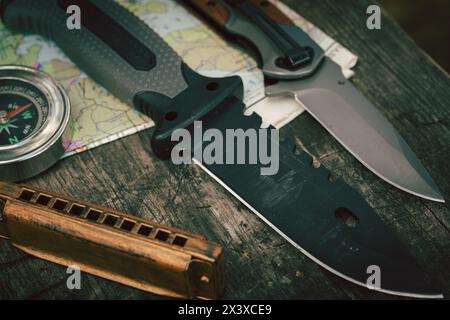 Adventures are waiting for you, knife, compass, harmonica, map spread out on wooden surface in forest Stock Photo
