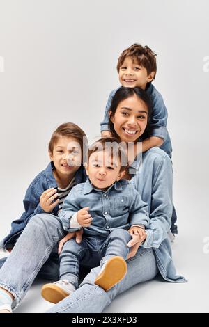 A young Asian mother and her little sons playfully stack on top of each other, all wearing denim clothes in a grey studio. Stock Photo