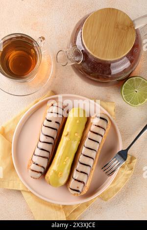Different tasty glazed eclairs and tea served on color textured table, flat lay Stock Photo