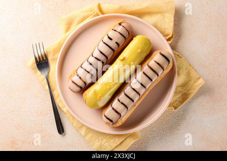 Different tasty glazed eclairs served on color textured table, top view Stock Photo