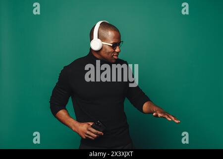 Young man with wireless headphones dances in a studio with a stylish green background, immersed in his happy playlist. His trendy moves and casual clo Stock Photo