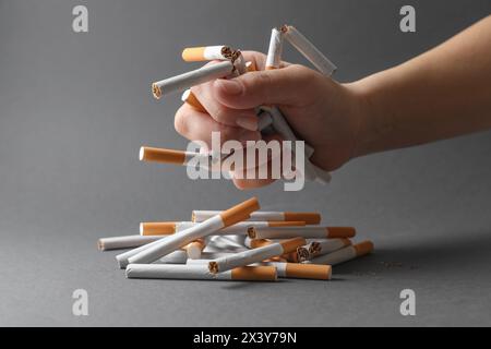 Stop smoking. Woman holding broken cigarettes over pile on grey background, closeup Stock Photo