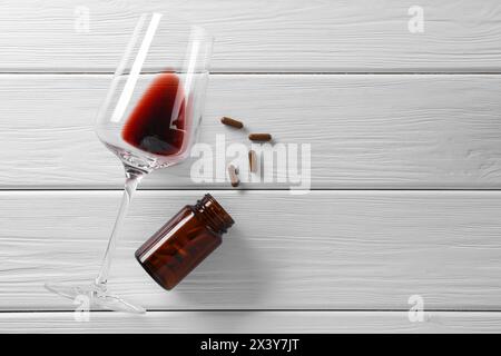 Alcohol and drug addiction. Glass with red wine, bottle and pills on white wooden table, flat lay. Space for text Stock Photo