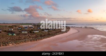 Aerial panorama landscape view of remote beach hut with a sea view on the Northumbrian sand dunes over looking Embleton Bay and Dunstanburgh Castle at Stock Photo