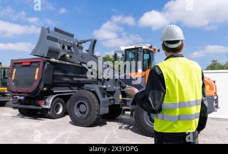 Engineer with a digital tablet on the background of construction machine. Stock Photo