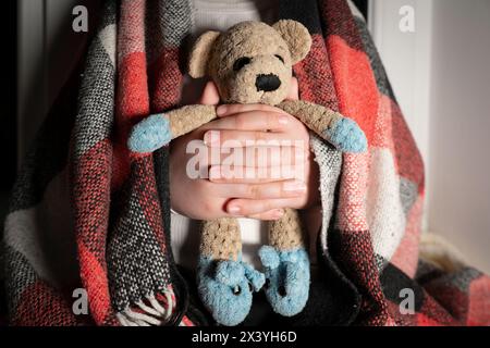 Blackout. Children's toy (teddy bear) in hands close-up. Power outages, destruction of energy infrastructure. Terror of civilians Stock Photo