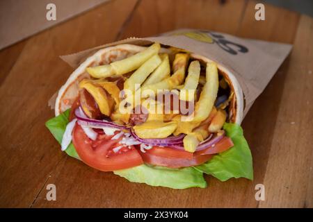 Tortilla wrap, a delightful fusion of savory sausages, crispy French fries, fresh green salad, juicy tomatoes, zesty onions, and shredded cabbage Stock Photo