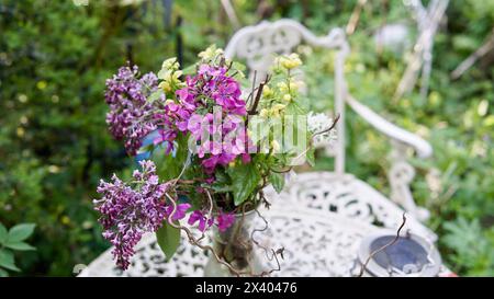Garden flowers in a vase on a white metal table. A white metal chair. Stock Photo