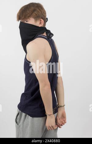 A Teenage Boy Wearing a Mask, Arrested in Handcuffs from Behind Stock Photo