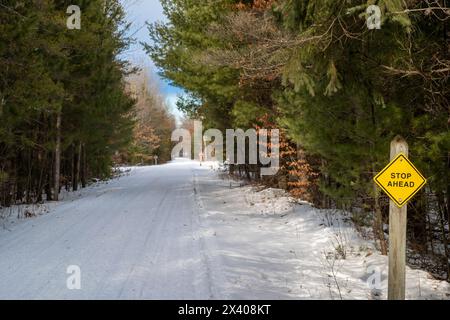Stop ahead sign on a snow covered snowmobile and hiking trail through a forest in Central Minnesota. Paul Bunyan State Trail in Nisswa. Stock Photo