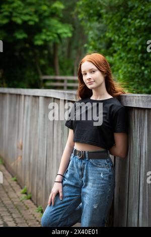 Red haired twelve year old girl with freckles posing leaning against a fence, Jette, Belgium. Model released. Stock Photo