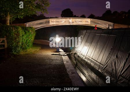 England, Northamptonshire, Braunston Marina entrance and Footbridge by Night with Moored Freight Narrowboat Stock Photo