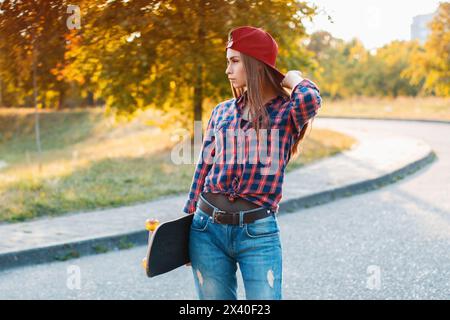 Young Stylish Girl With Skateboard Standing In The Park On A Sunny Day Stock Photo