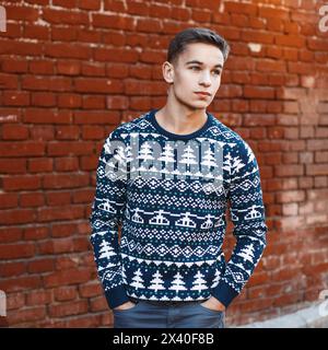 Young Handsome Man In A Knit Sweater With Christmas Ornaments On A Background Of Red Brick Wall Stock Photo