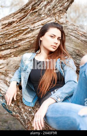 Fashion Portrait Of A Beautiful Young Girl In Denim Dress On A Background Of A Tree Stock Photo