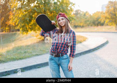Beautiful Young Hipster Girl In Stylish Clothes Holding A Skateboard And Smiling At Sunset Stock Photo