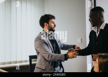 Two diverse professionals celebrating success with a handshake in a modern office setting Stock Photo