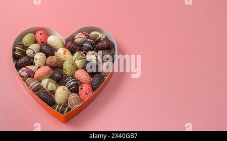 Chocolate Easter eggs in a heart-shaped box on a pink background with copy space. Stock Photo
