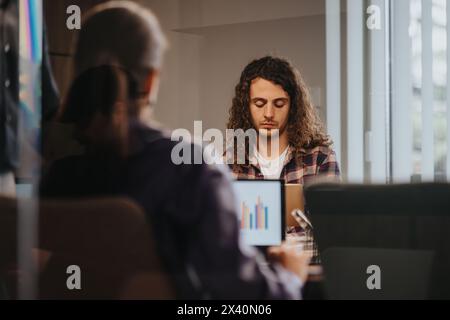 Young entrepreneurs in a meeting room discussing growth and investments, using graphs on a tablet Stock Photo