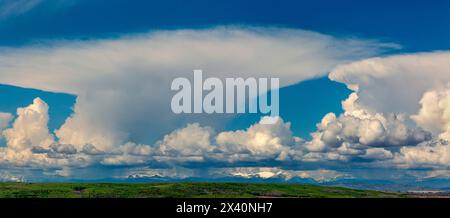 Panorama of storm clouds over the mountains and green foothills with blue sky, West of Calgary, Alberta; Alberta, Canada Stock Photo