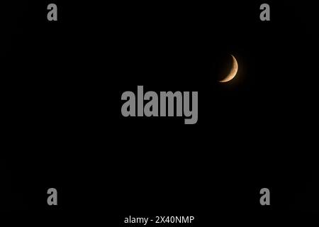 Crescent moon glowing with the warm light of the sun in a black sky; Calgary, Alberta, Canada Stock Photo