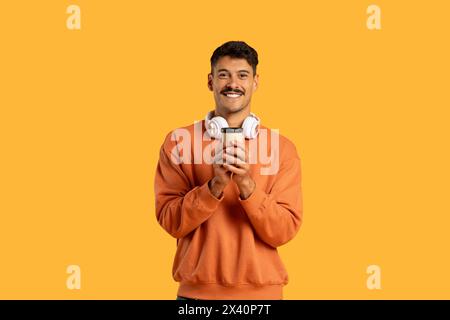 Smiling Man in Orange Sweatshirt Holding a Cup and Headphones Stock Photo