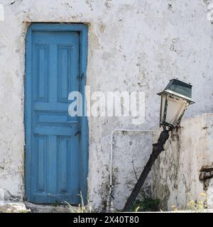 Broken lamp post beside a blue door on a dirty whitewash house in Greece; Ano Mera, South Aegean, Greece Stock Photo