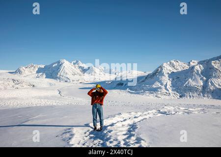 Teenage girl wearing an orange sweater and jeans standing on a glacier and holding her sunglasses; Palmer, Alaska, United States of America Stock Photo