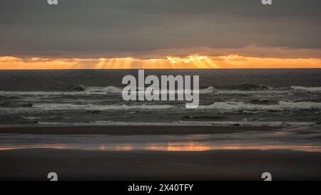 Beautiful sunset with fingers of God extending down from behind the clouds over the Pacific Ocean from the beach at Cape Disappointment State Park ... Stock Photo