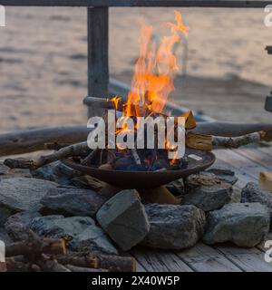 Fire burns in a fire pit on a dock; Lake of the Woods, Ontario, Canada Stock Photo