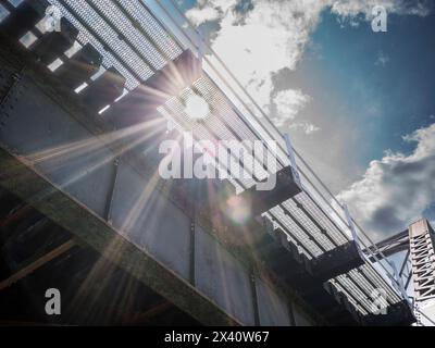 Bright sunlight shining through a bridge structure with sun rays and lens flare, and a view to the sky with clouds; Lake of the Woods, Ontario, Canada Stock Photo