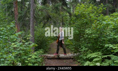 Woman balances on a log across a hiking trail in a forest, Boyne Lake Trail; Ontario, Canada Stock Photo