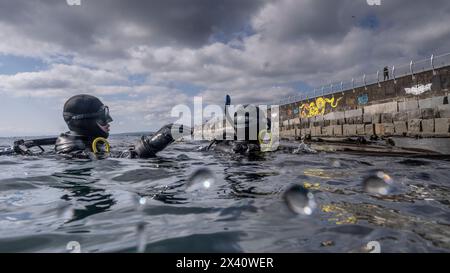 Scuba divers in gear in the water beside a wall with graffiti, with water droplets on the lens of the camera; Lake of the Woods, Ontario, Canada Stock Photo