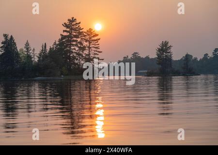 Dramatic sunset light over a lake with silhouetted trees along the shoreline and a sunbeam reflected on the water's surface Stock Photo