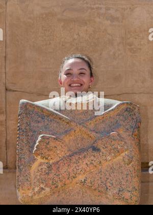 Girl posing as ancient Egyptian god with headless statue at the Karnak Temple in Luxor, Egypt; Luxor, Egypt Stock Photo