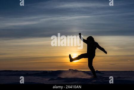 Silhouette of a young man kicking the snow on a winter sunset at the beach; Anchorage, Alaska, United States of America Stock Photo