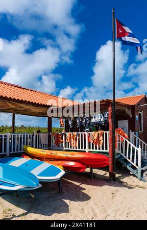 Beachfront recreation with kayaks, surfboards and lifejackets outside a building with a Cuban flag; Cay Guillermo, Cuba Stock Photo