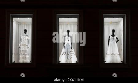 Haute couture fashion, white floor-length bridal gowns, on display on dark skinned mannequins in illuminated bridal shop windows at night Stock Photo