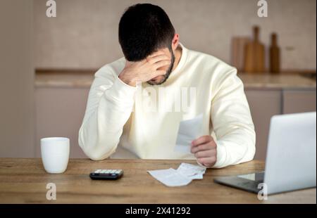 Upset Man Sitting at Table With Head in Hands Stock Photo