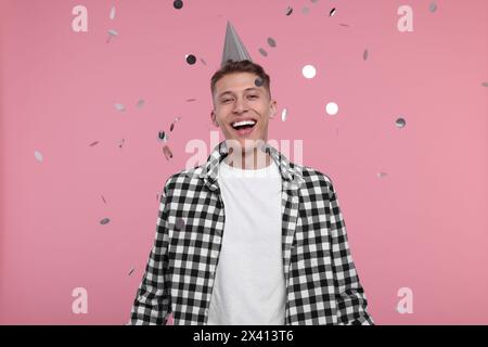 Happy man in party hat under falling confetti on pink background Stock Photo