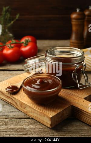 Tasty barbeque sauce in bowl, jar and spoon on wooden table Stock Photo