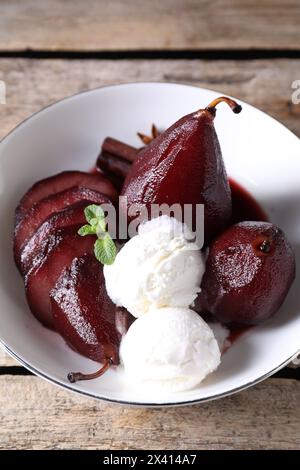 Tasty red wine poached pears and ice cream in bowl on wooden table, above view Stock Photo