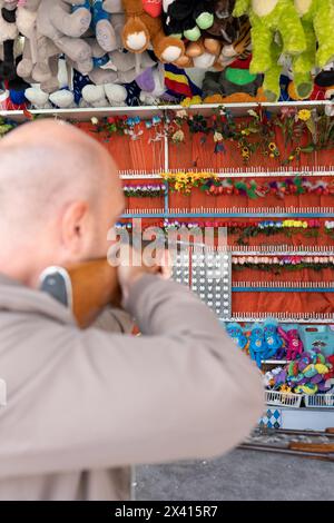 A rear view of a tourist playing shooting games to win plush toys on the wall at the fair. Shooting games. Stock Photo