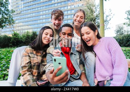 Excited multiracial group of friends enjoying and smiling using a cellphone app. Diverse teenagers having fun watching content on the social media with a smartphone outdoors. Young people with phone. High quality photo Stock Photo
