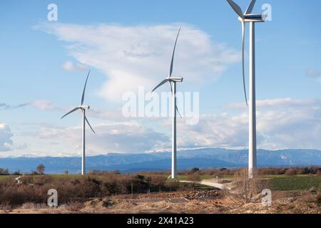 Three wind turbines are standing in a field with a cloudy sky in the background. Scene is calm and peaceful, as the turbines are not in motion and the Stock Photo