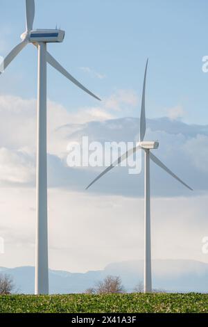 Two wind turbines are standing in a field with a cloudy sky in the background. The turbines are tall and white, and they are the only structures visib Stock Photo