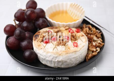 Plate with tasty baked camembert, honey, grapes, walnuts and pomegranate seeds on white tiled table, closeup Stock Photo