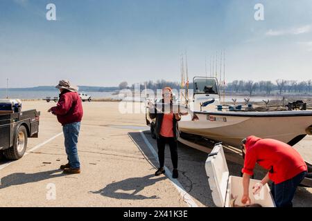 Caucasian woman displays her catfish catch standing next to fishing boat. Two other people in picture. Oklahoma, USA. Stock Photo