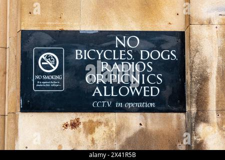 Sign prohibiting bicycles, dogs, radios, and picnics on the wall of Kings College, Cambridge University, with a no smoking symbol and CCTV notice. UK Stock Photo